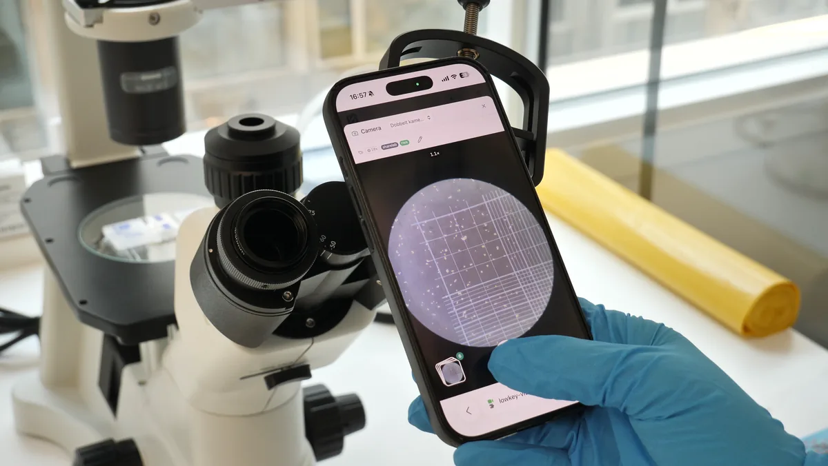 A phone held to the eyepiece showing the hemocytometer grid live in the app